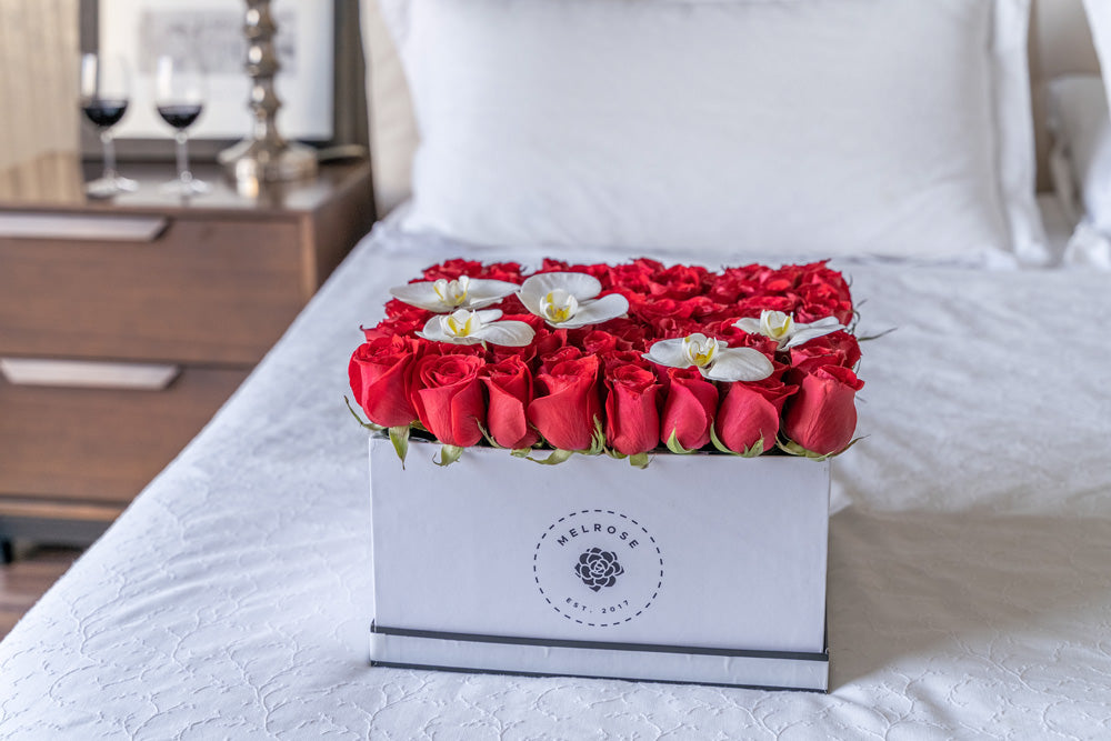 Rosas rojas en caja con flores de orquídea