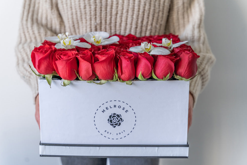 Rosas rojas en caja con flores de orquídea