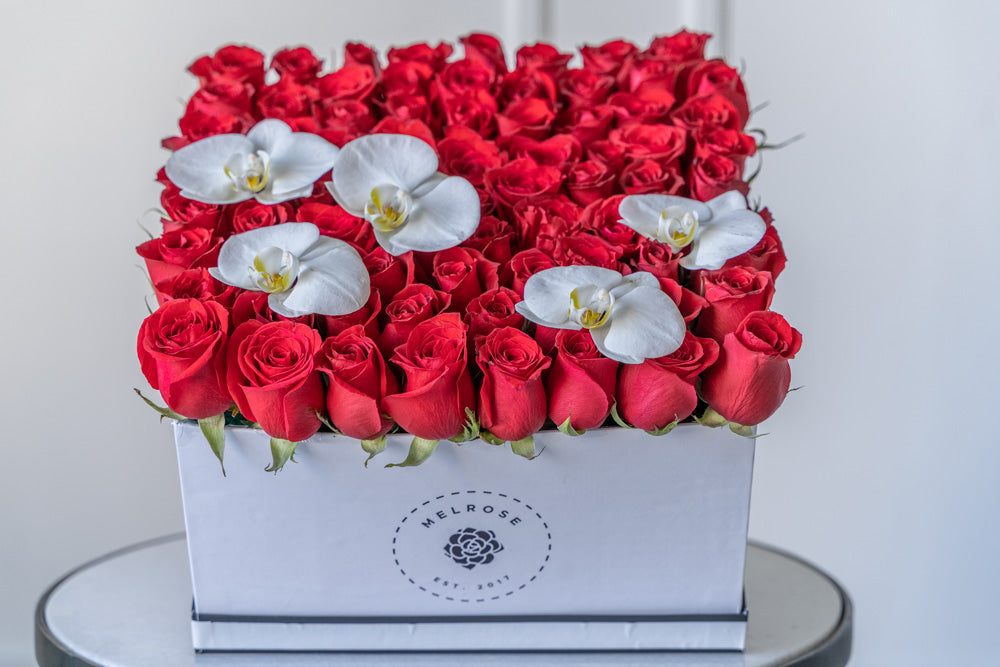 Rosas rojas en caja con flores de orquídea